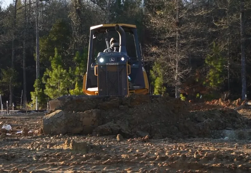 Dozer pushing red clay across a pad being cut on a wooded site