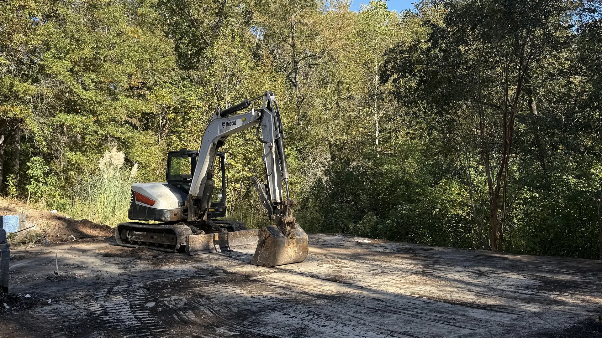 Excavator parked on a cleared gravel pad at the edge of the woods