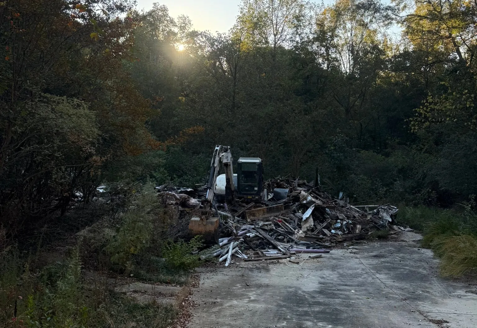 Excavator working a pile of demolition debris at the end of a concrete driveway at sunset
