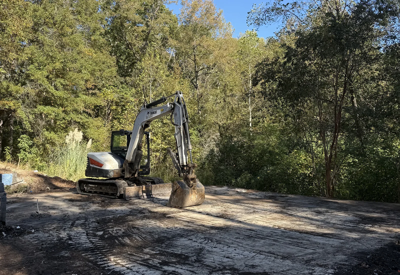 Excavator parked on a cleared gravel pad edged by woods after the debris was hauled off