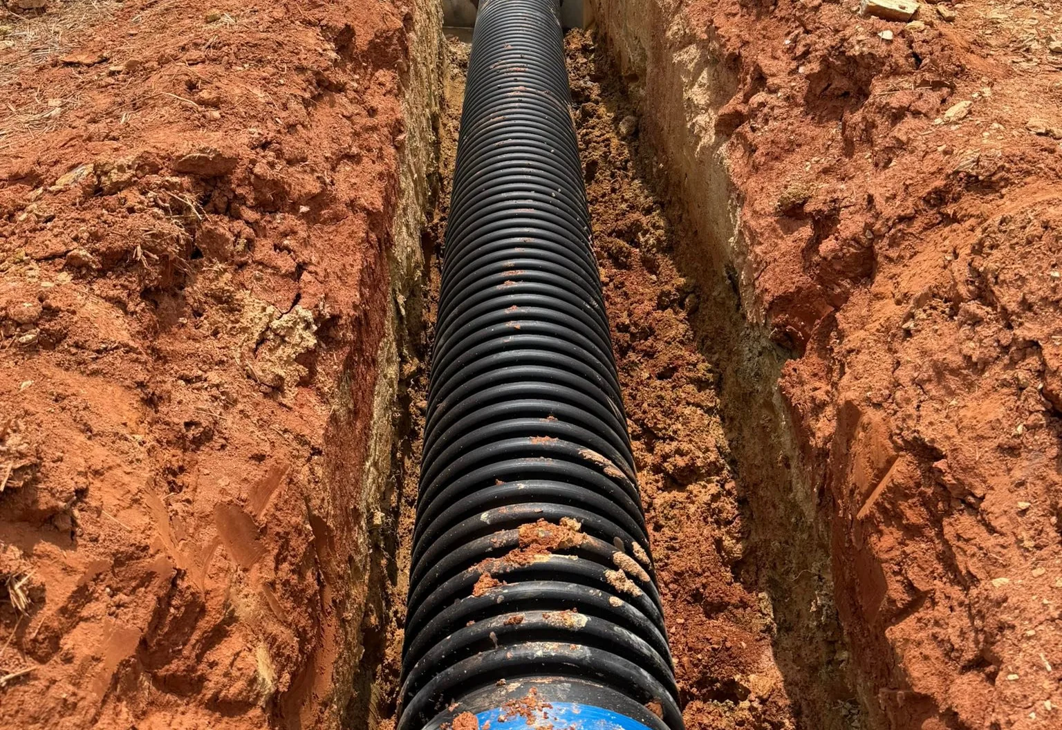Corrugated drain pipe laid in an open trench cut through red clay