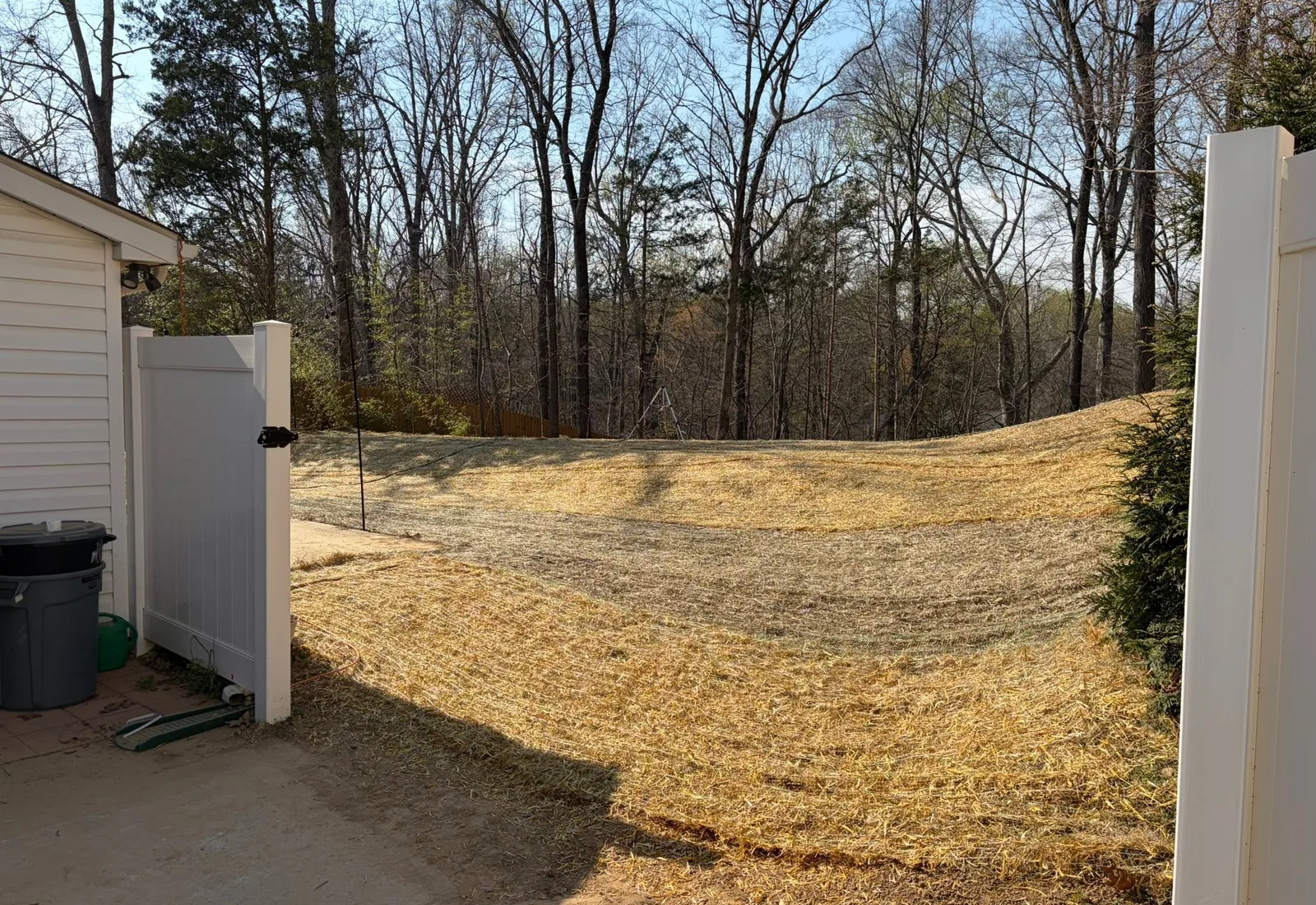 Regraded yard covered in straw sloping away from a house toward a fence line