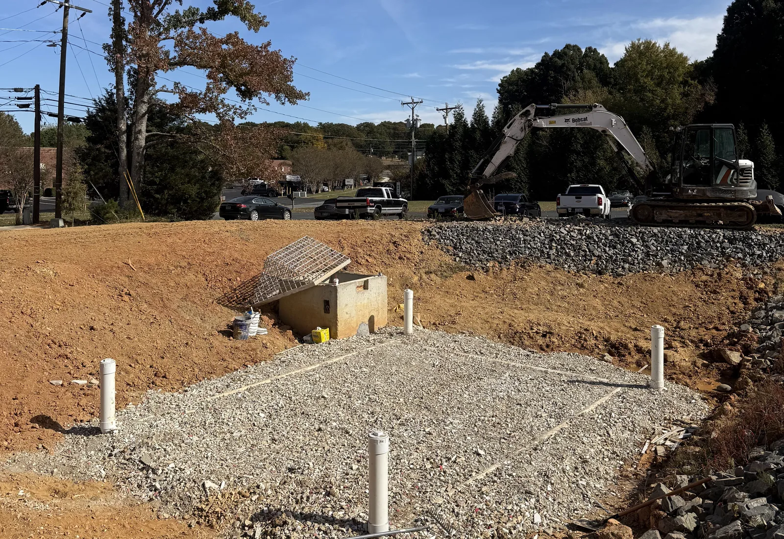 Gravel bed with pipe risers and rock built into a drainage structure, excavator working behind it