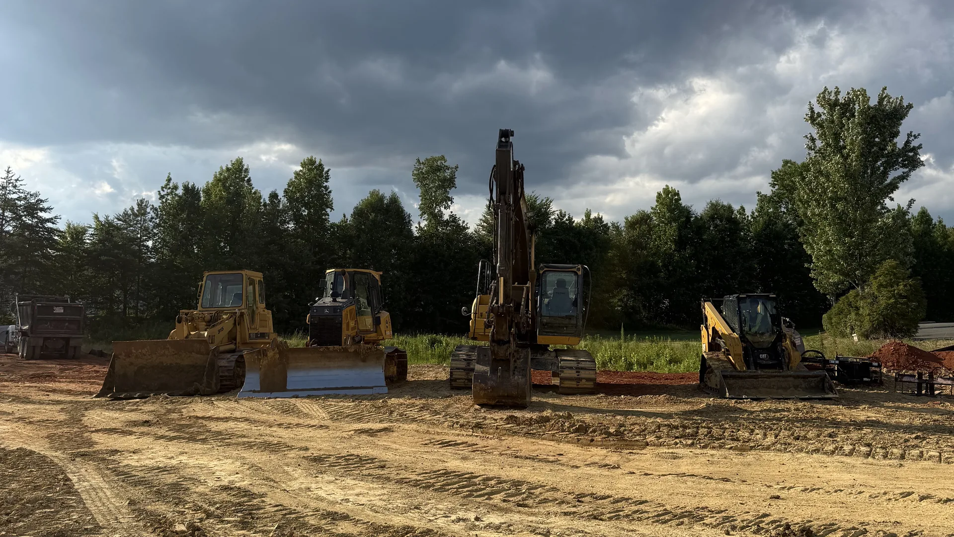 Four machines lined up on a large graded pad under storm clouds