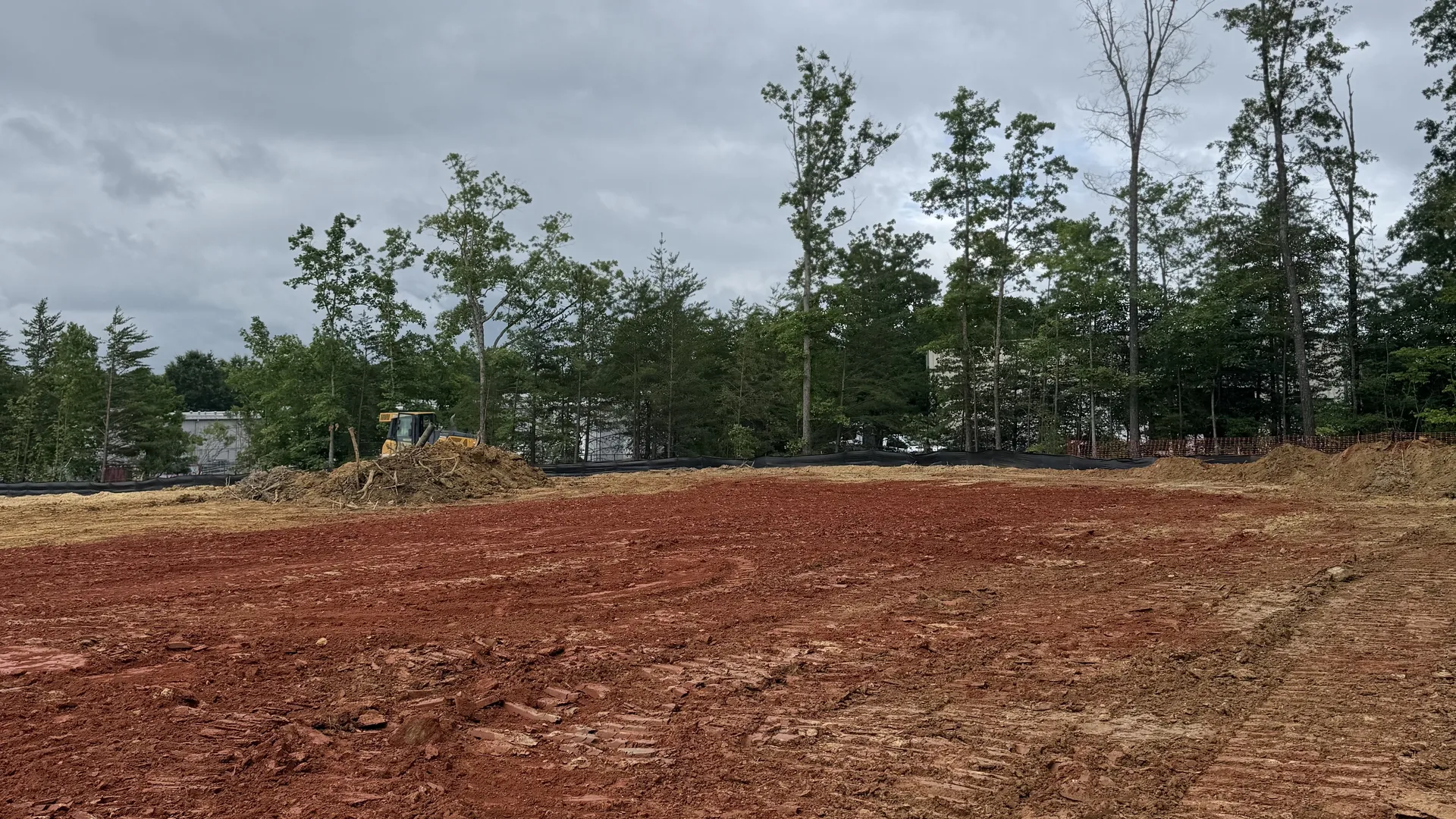 Wide red clay lot cut to grade with a dozer working at the tree line