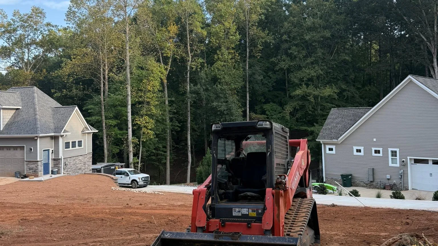 Compact track loader on a red clay pad between two new houses in a subdivision