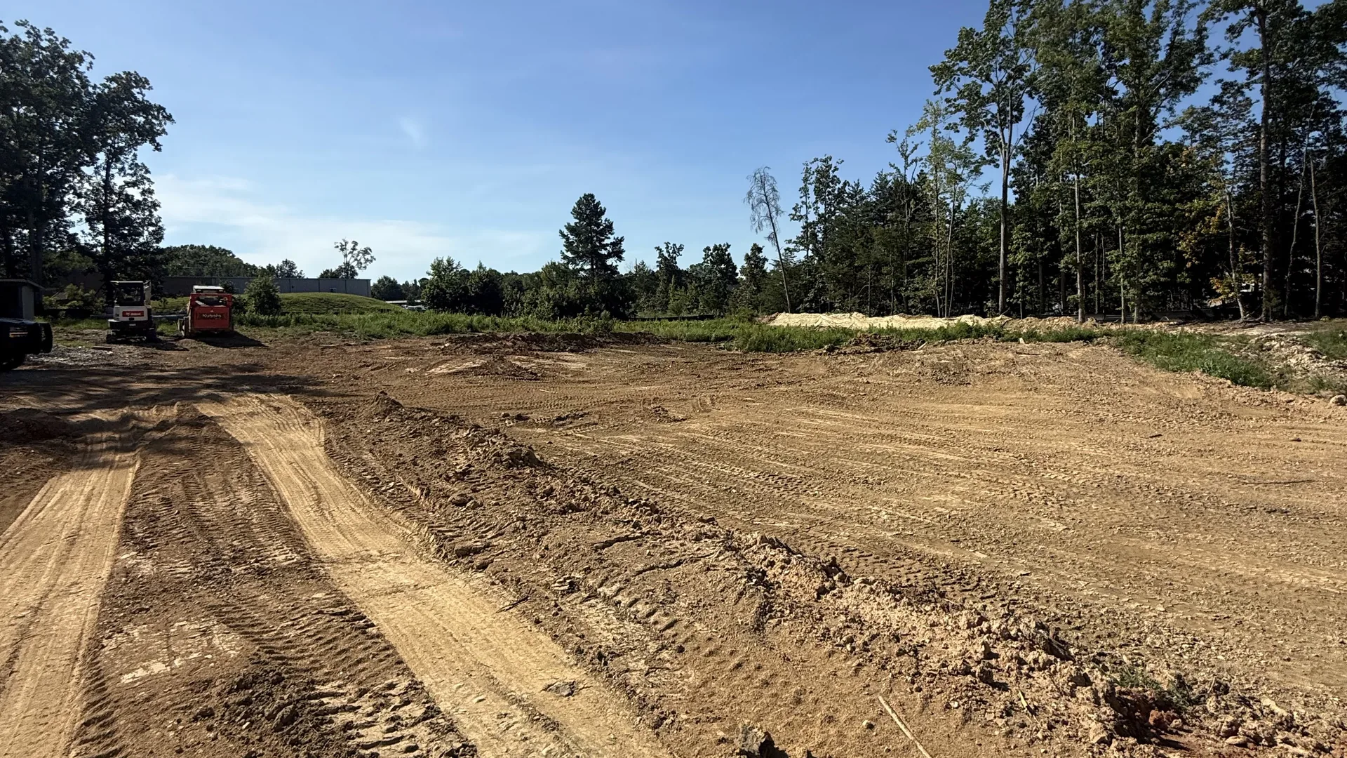 Graded dirt pad running back to the woods with equipment working at the far end