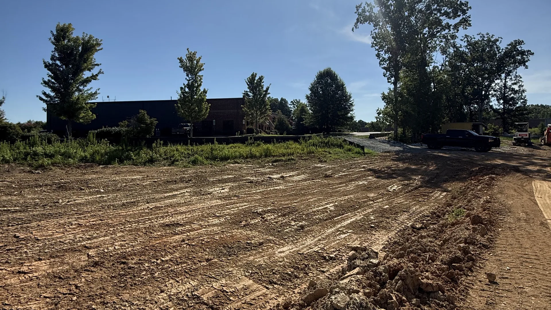 Freshly cut and graded lot beside a commercial building under a bright sun