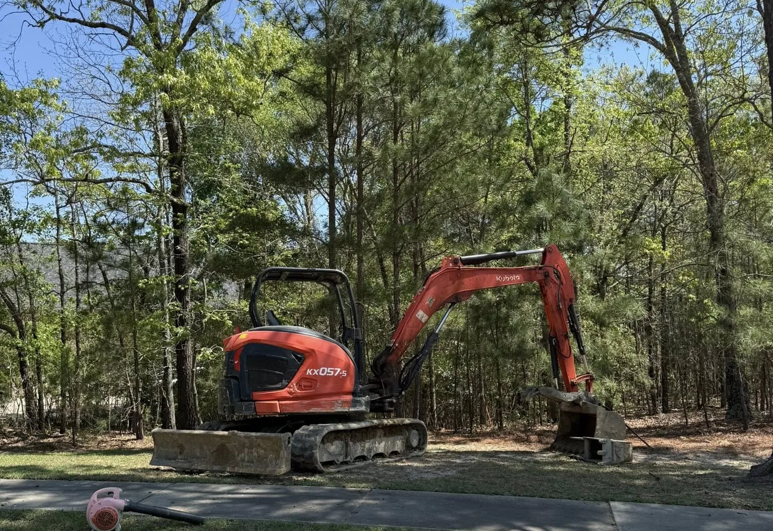 Mini excavator clearing brush and small trees among pines on a wooded lot