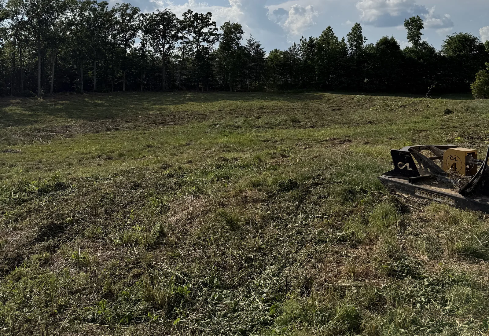 Freshly mulched field with the forestry mulcher head resting on the cut ground and the tree line left standing