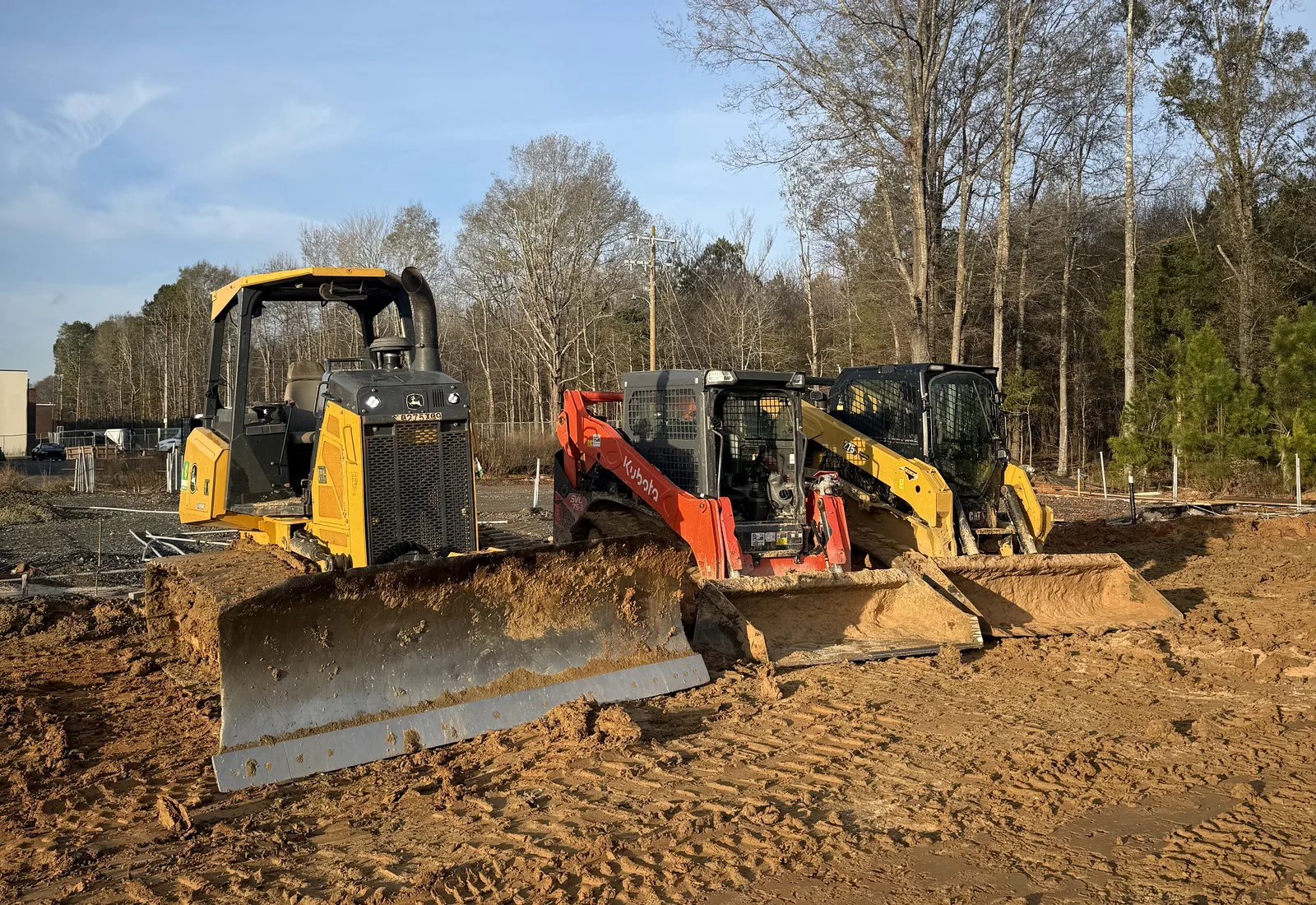 Dozer and compact track loader shaping a red clay building pad under an open sky