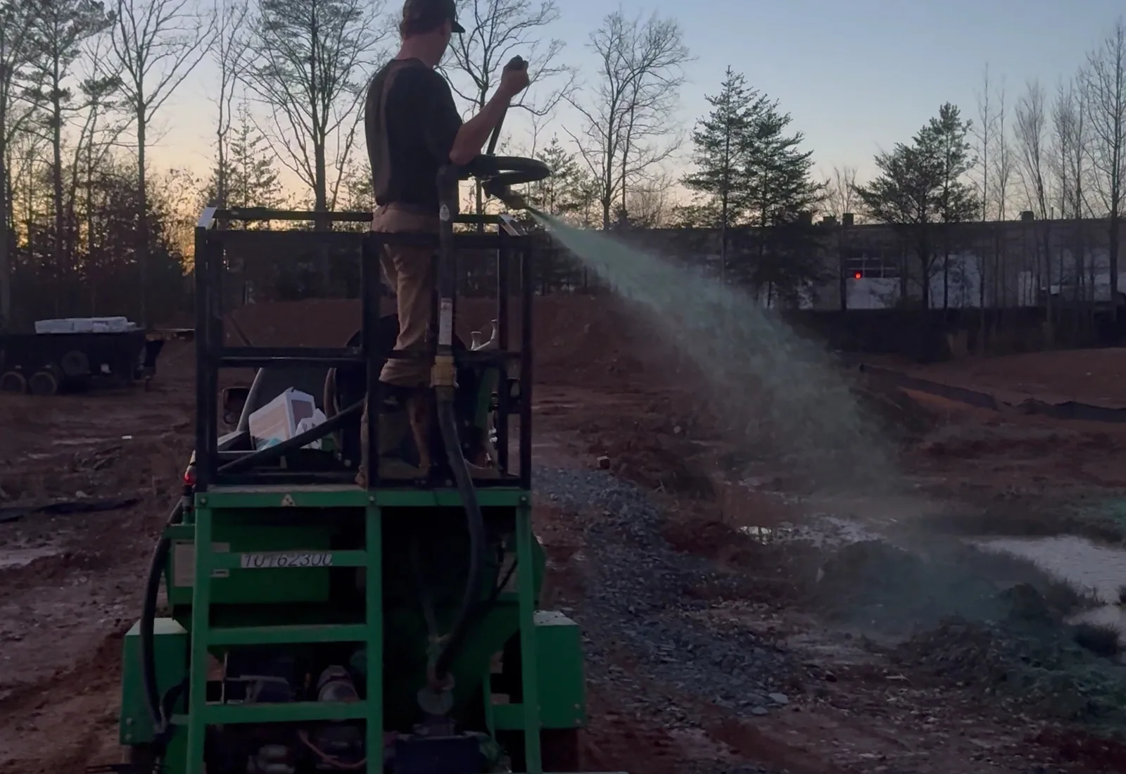 Hydroseeder spraying green mulch across a freshly graded pad at dusk