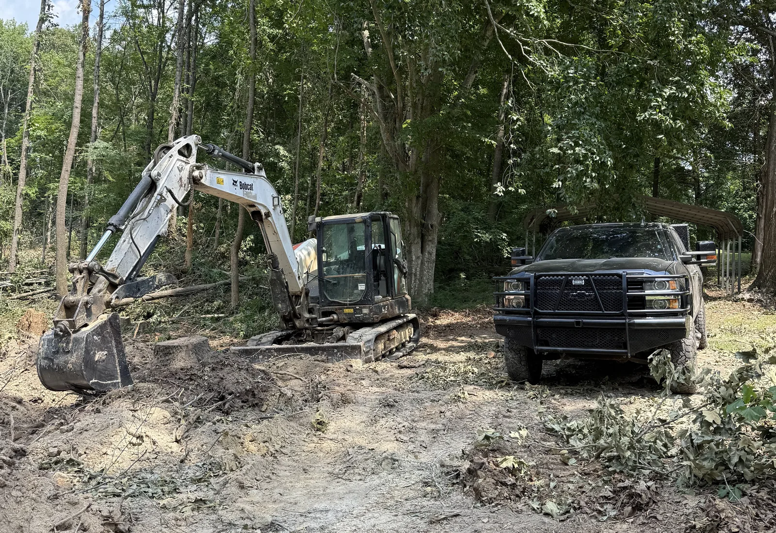 Excavator and pickup truck clearing brush along a tree line in hardwoods
