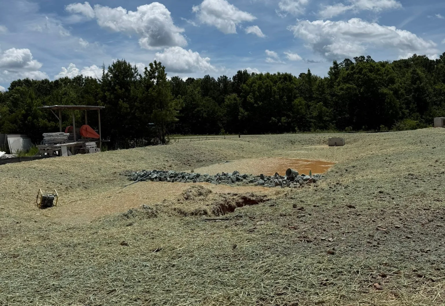 Graded basin lined with rock in a straw covered field with water standing in the bottom