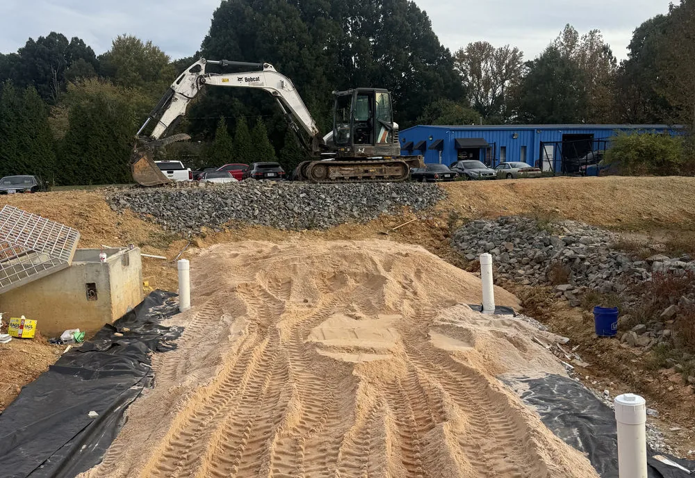 Sand filter bed with pipe risers built into a basin, excavator parked on the bank behind it