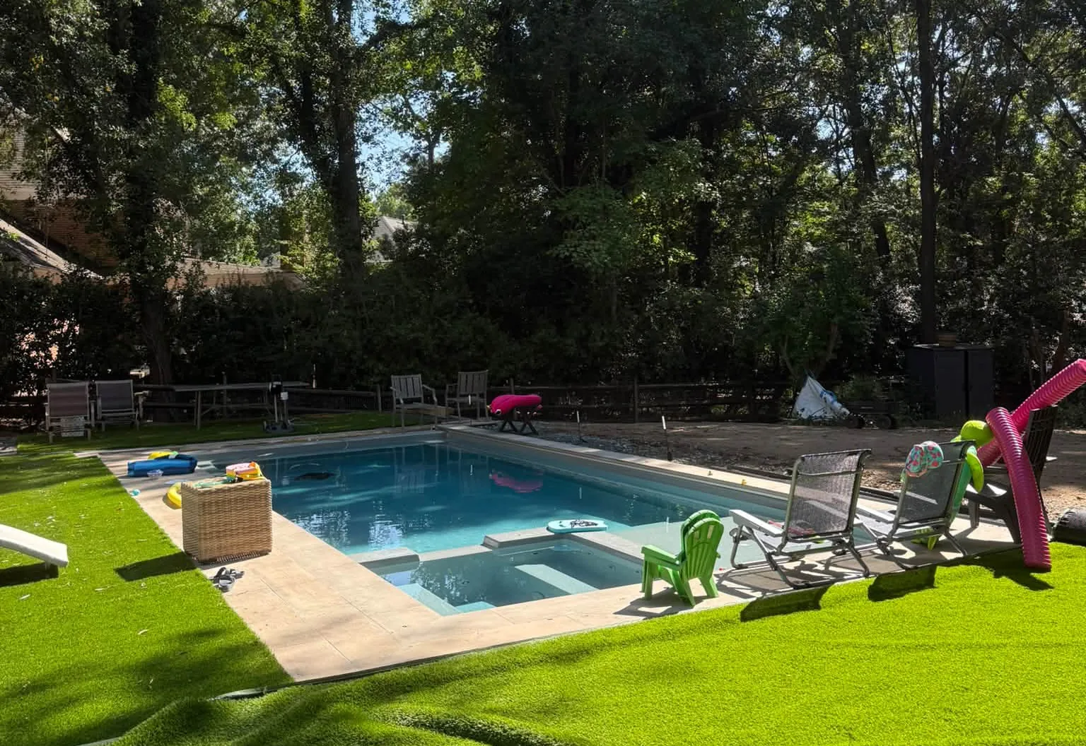 Finished inground pool with a tanning ledge behind a two-story house, new turf and patio chairs around it