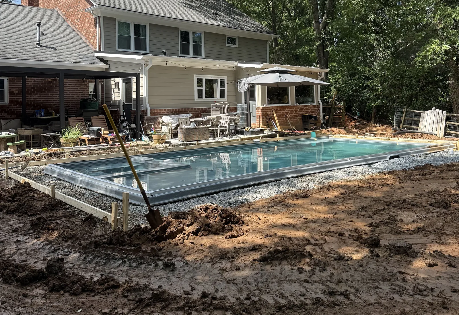 New inground pool behind a two-story house with the yard around it stripped and graded for the deck