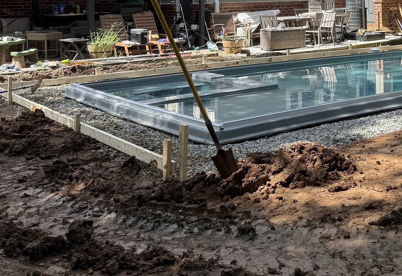 Inground pool shell set on a gravel bed with timber forms around the edge, bare dirt and a shovel in the foreground