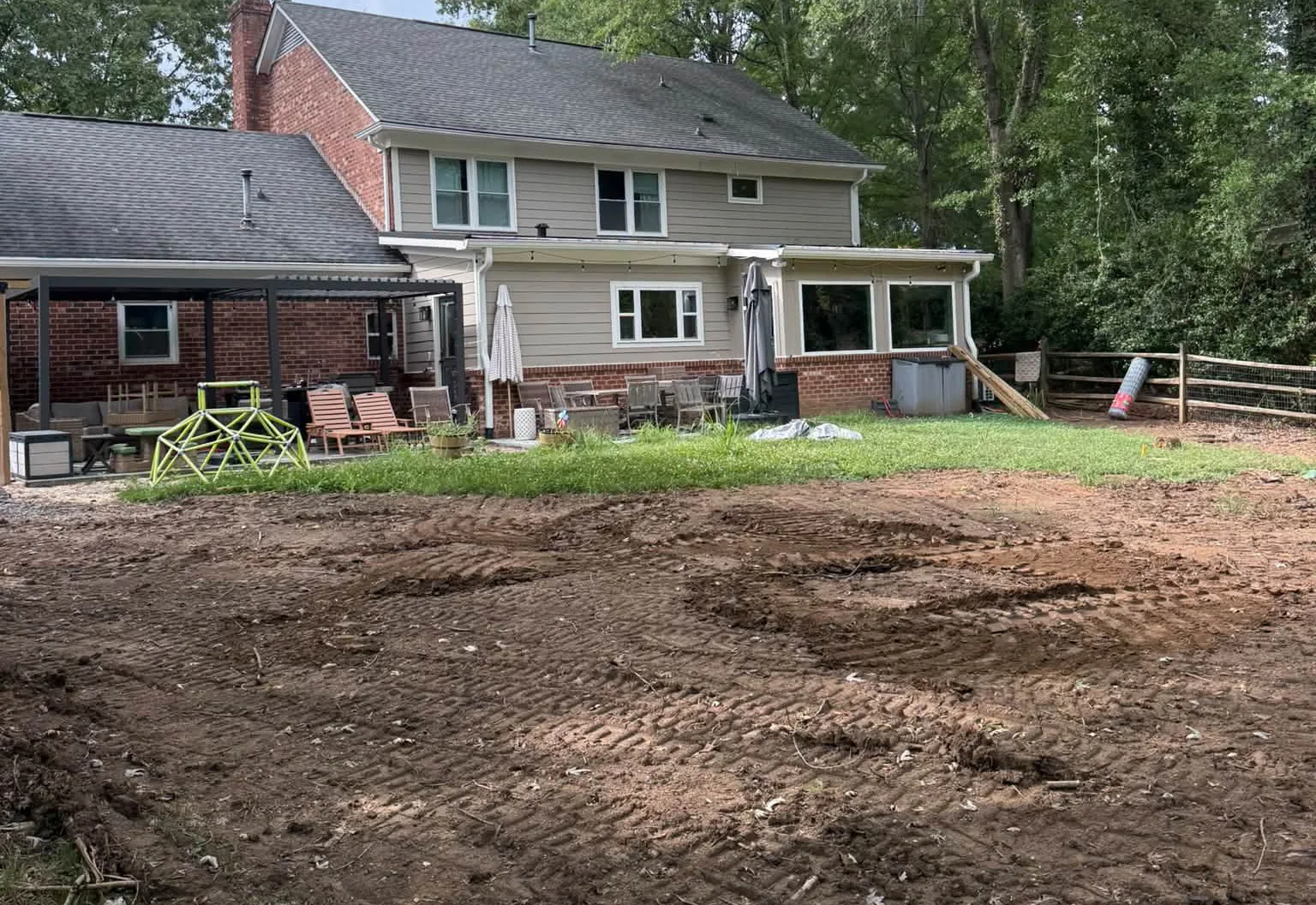 Backyard stripped to bare dirt behind a two-story house with a covered patio
