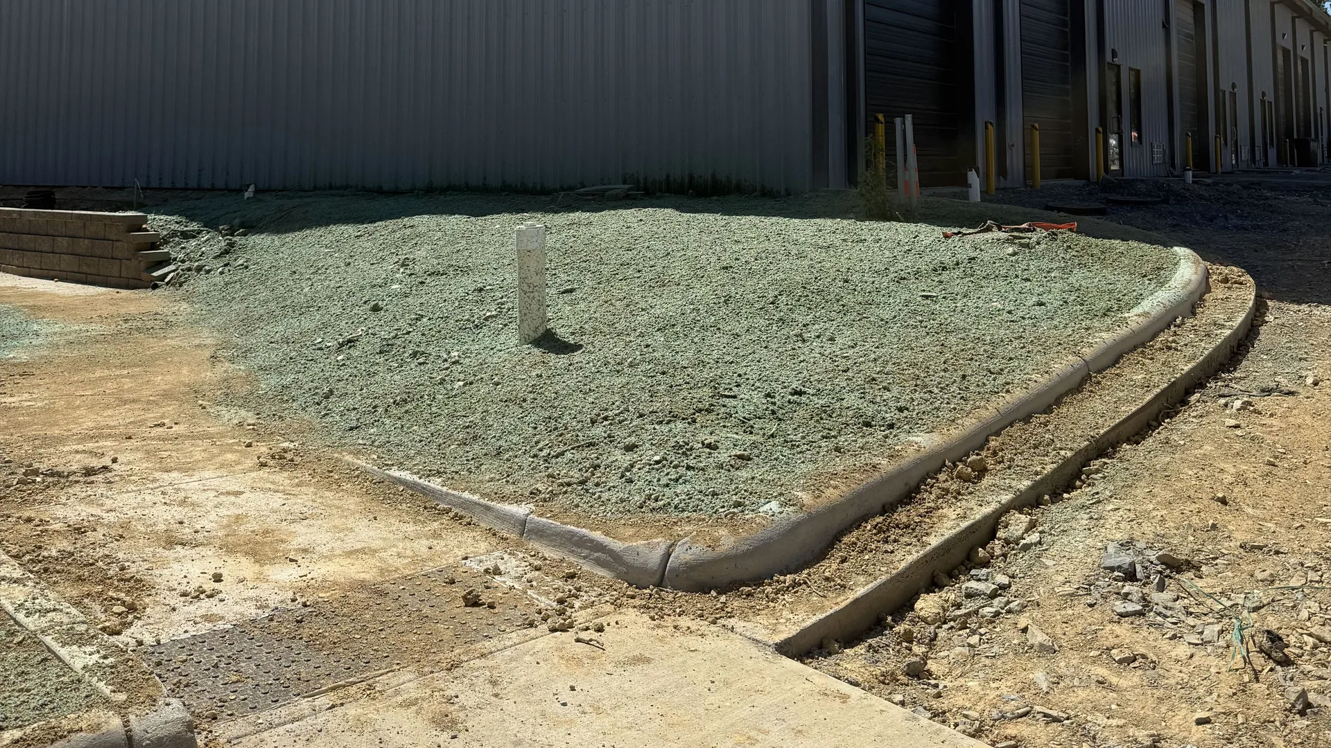 Hydroseeded strip inside a new concrete curb beside a metal commercial building with a concrete apron