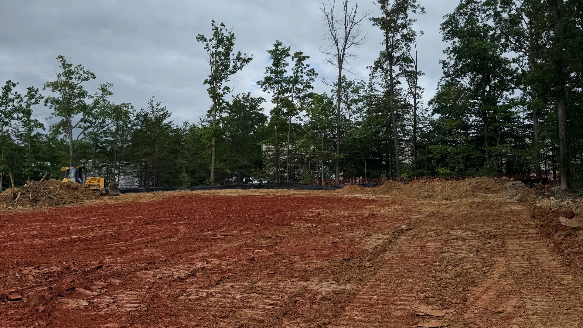 Wide red clay lot graded flat with a dozer working along the tree line
