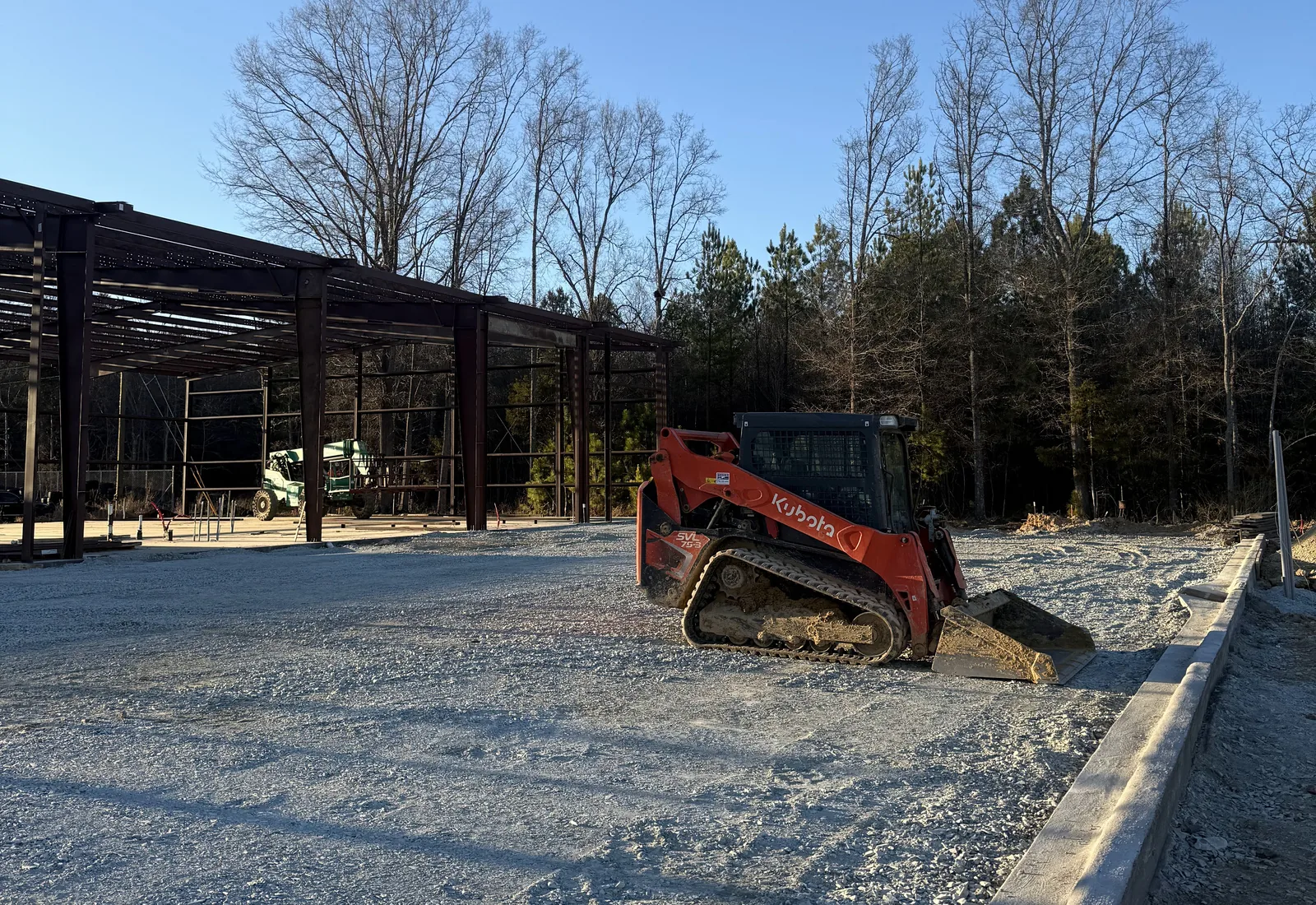Compact track loader on a new gravel lot beside a steel framed commercial building with fresh curbing