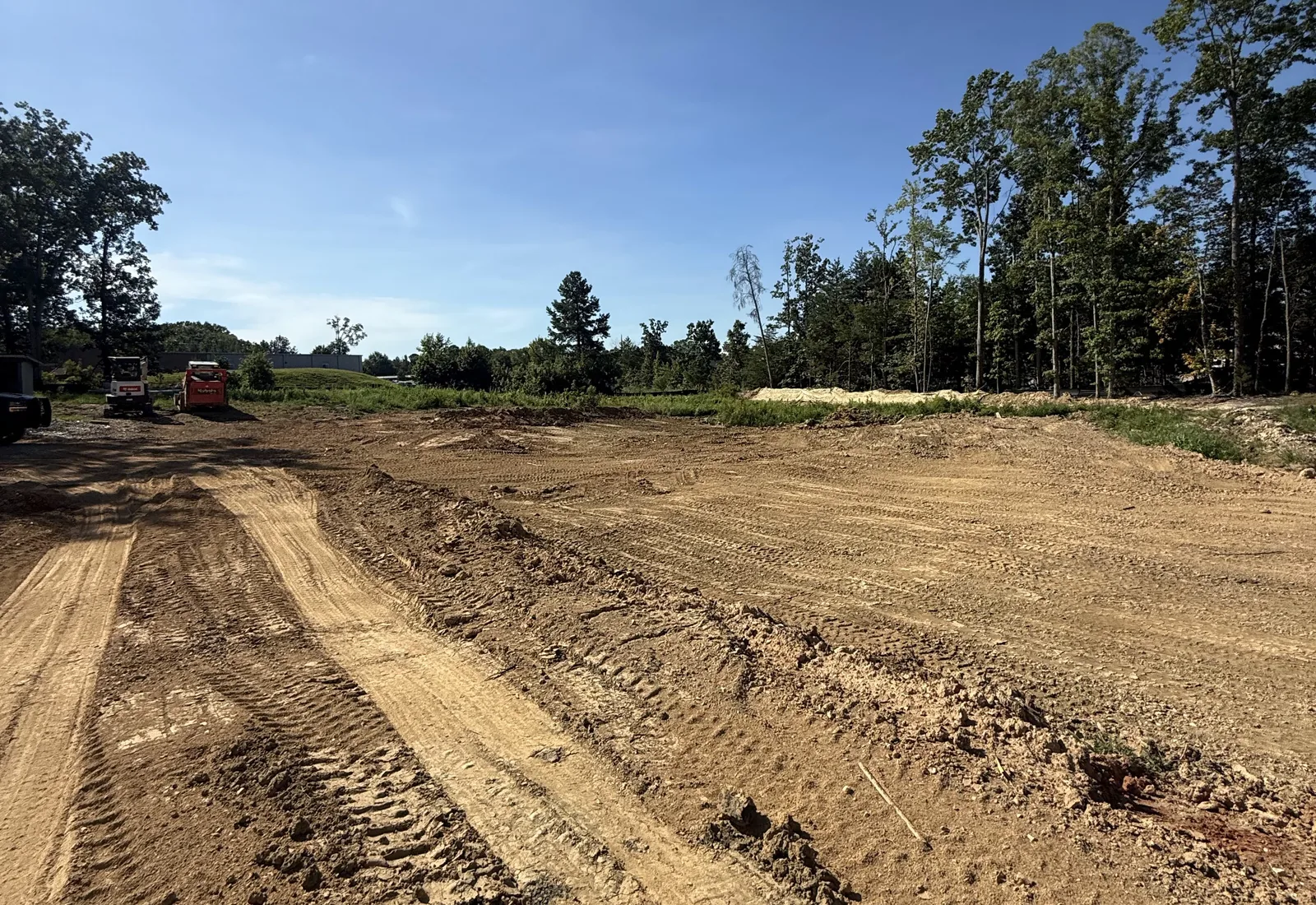 Wide graded building pad running back to the woods with tracked equipment at the far end