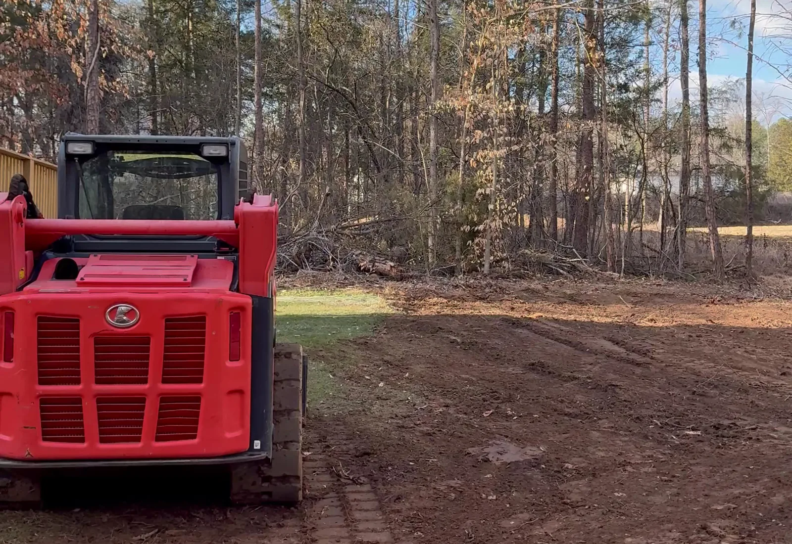 Compact track loader on a freshly graded red clay pad in a stand of pines
