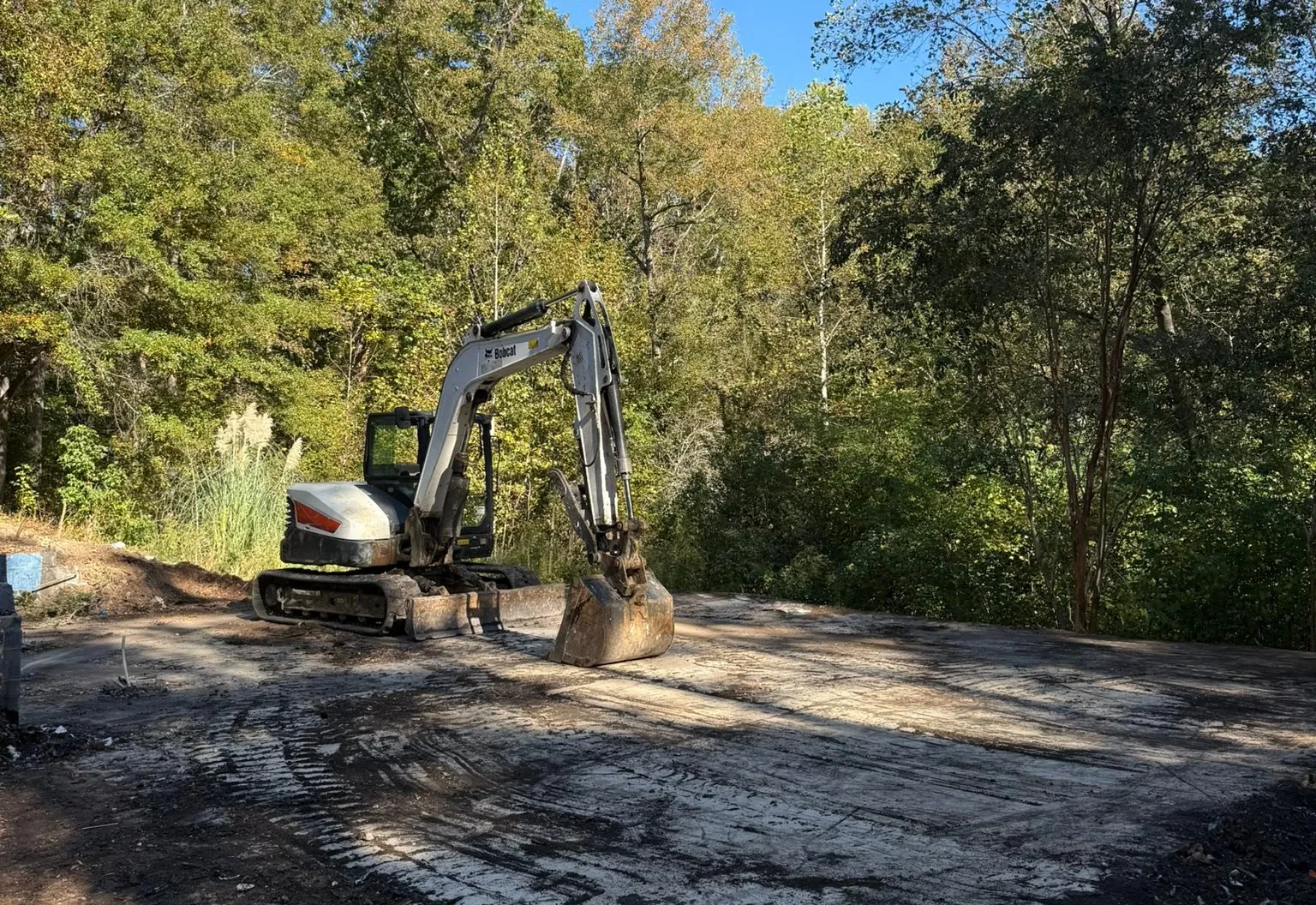Excavator on a cleared lot at the edge of the woods
