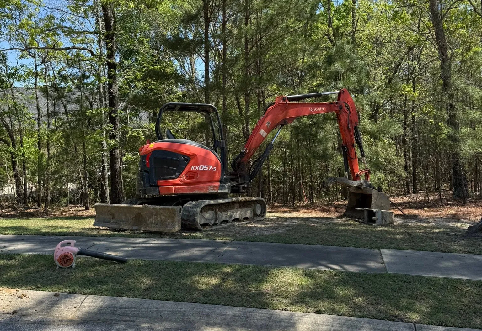 Orange mini excavator parked on the grass beside a residential street